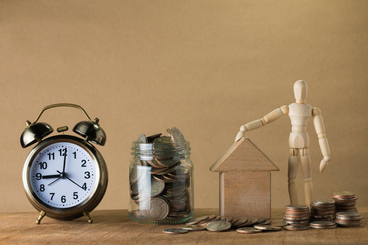 Wooden mannequin with a house, coins, and clock symbolizing time and financial planning.