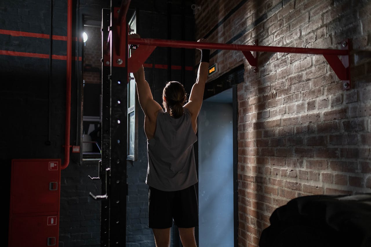 Man in activewear doing pull-ups in an indoor gym setting, emphasizing fitness and well-being.
