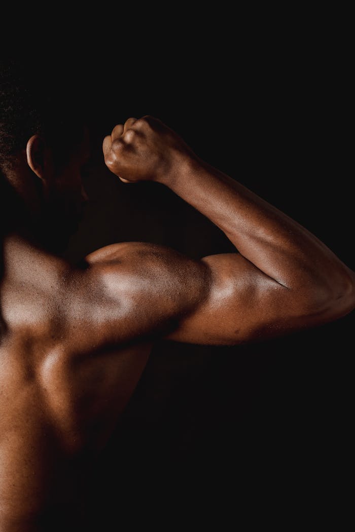 Portrait of a shirtless man flexing his arm, highlighting defined muscles in a dramatic lighting.